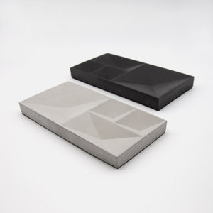 May include: Two rectangular concrete trays with geometric designs. One tray is gray and the other is black.