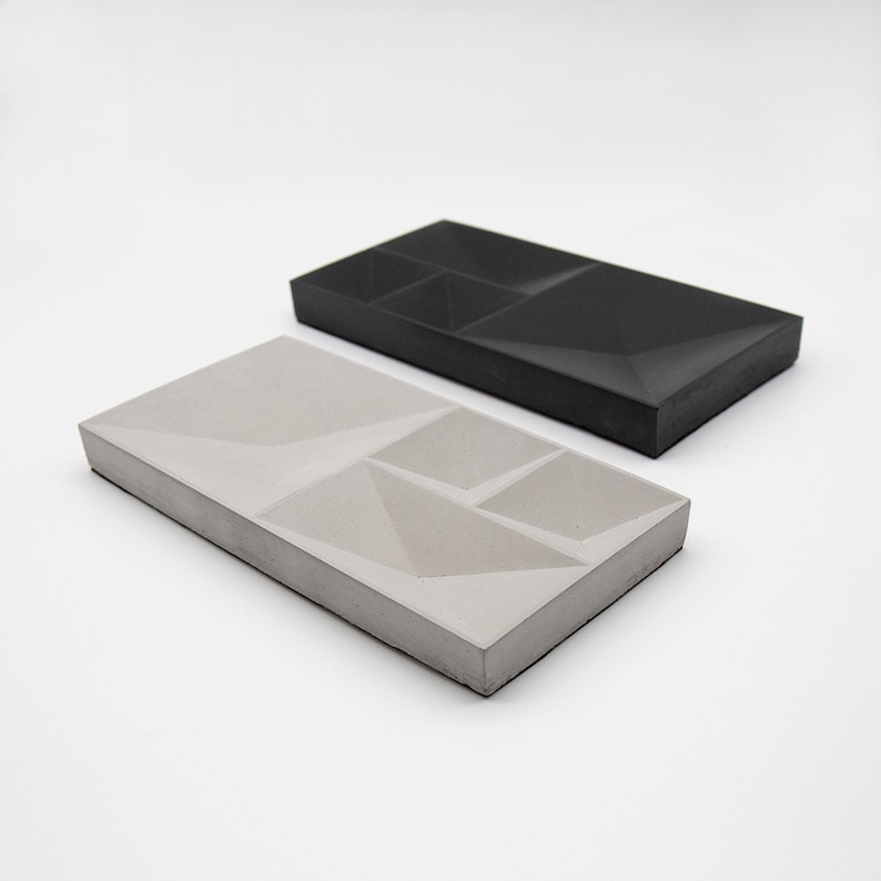 May include: Two rectangular concrete trays with geometric designs. One tray is gray and the other is black.