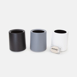 May include: Three cylindrical containers, one black, one gray, and one white. The containers are made of a smooth, matte material and have a simple, modern design. The containers are all the same size and shape.