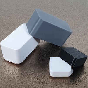 May include: Four small, square boxes in different colors. Two are white, one is black, and one is gray. The boxes are stacked on top of each other.