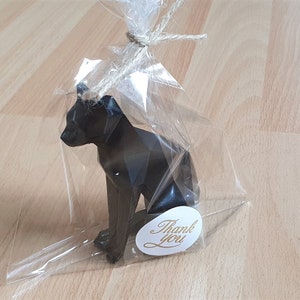 Könnte beinhalten: Eine schwarze Origami-Katzenfigur mit geometrischem Design. Die Katze sitzt auf einer weißen Oberfläche mit einem Dankeschön-Etikett.