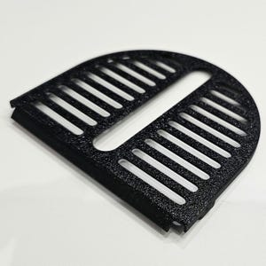 Op de afbeelding: Een zwarte, halfronde ventilatieafdekking met een getextureerd oppervlak en een reeks parallelle sleuven. Het ontwerp heeft een centrale rechthoekige opening en een afgeronde rand, geschikt voor diverse toepassingen.