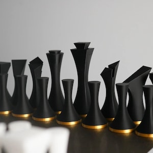 Op de afbeelding: Een set zwarte schaakstukken met gouden accenten. De stukken zijn gemaakt van glad, mat materiaal en hebben een modern, minimalistisch ontwerp.