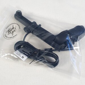 Puede incluir: Un cable eléctrico negro con un enchufe y un dispositivo negro con una pequeña cámara en el extremo. El dispositivo está empaquetado en una bolsa de plástico transparente con una pegatina que dice "¡Gracias!" en letras negras.