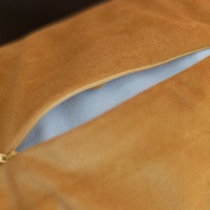 A close-up of a mustard yellow WELLB crescent cushion, showcasing a partially opened zipper revealing an inner lining. The soft, suede-like fabric adds a luxurious texture. A high-quality, refillable design for comfort, yoga, and mindfulness.