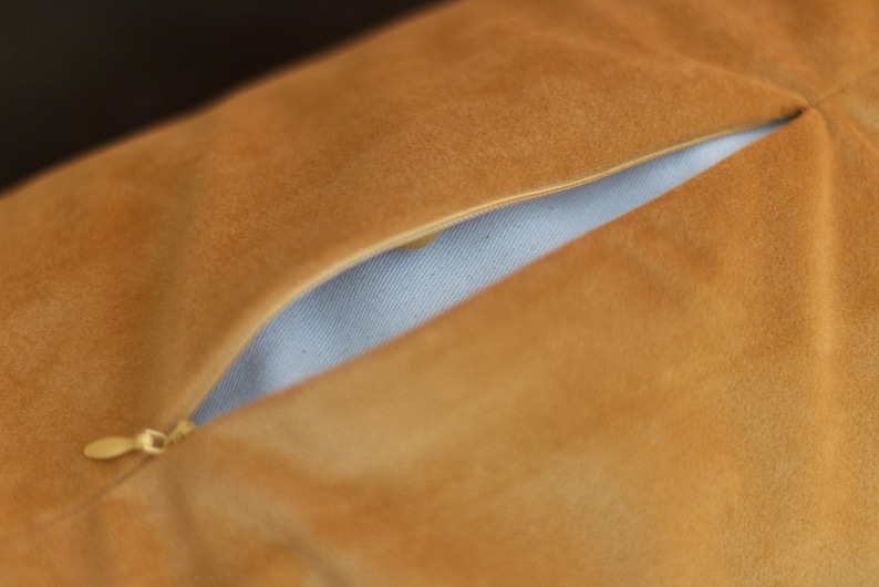 A close-up of a mustard yellow WELLB crescent cushion, showcasing a partially opened zipper revealing an inner lining. The soft, suede-like fabric adds a luxurious texture. A high-quality, refillable design for comfort, yoga, and mindfulness.