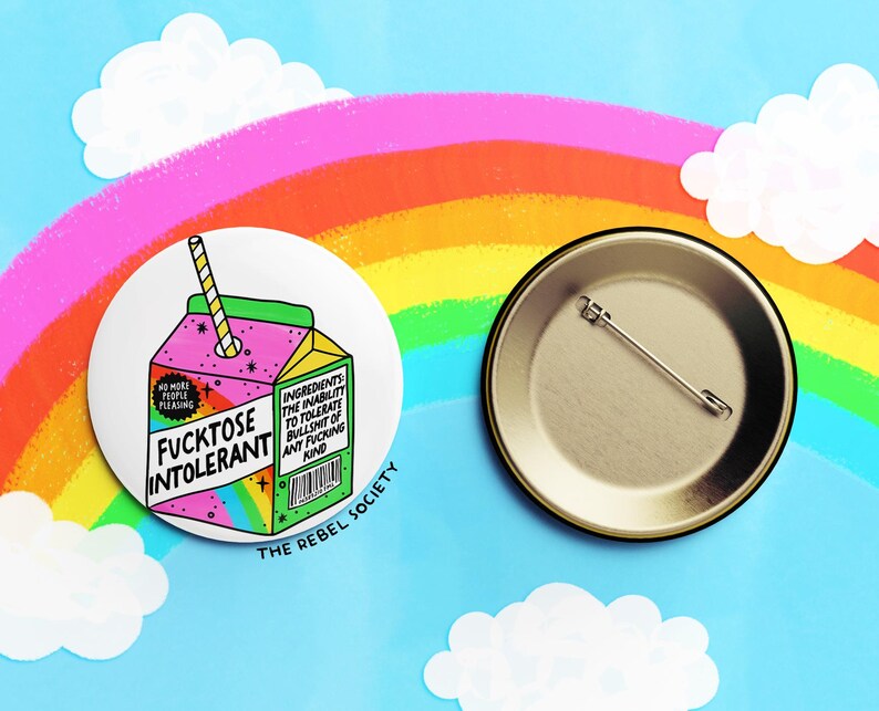 May include: A round button featuring a cartoon illustration of a juice carton with a straw. The juice carton is pink and green with a rainbow design. The text on the juice carton reads "Fucktose Intolerant". The button is white with a black border and the text "The Rebel Society" printed below the image.