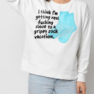 May include: White sweatshirt with a blue graphic of two socks and the text "I think I'm getting real fucking close to a grippy sock vacation."