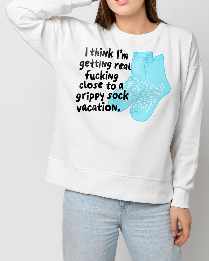 May include: White sweatshirt with a blue graphic of two socks and the text "I think I'm getting real fucking close to a grippy sock vacation."