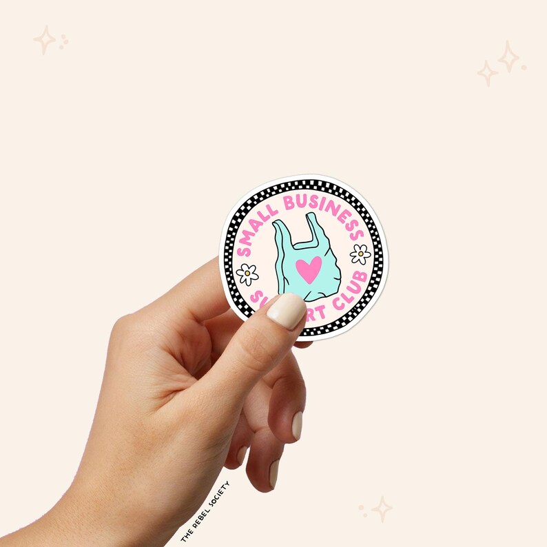 May include: A round sticker with the text "SMALL BUSINESS SUPPORT CLUB" in a black and white border. The sticker features a light blue shopping bag with a pink heart in the center and small white flowers.