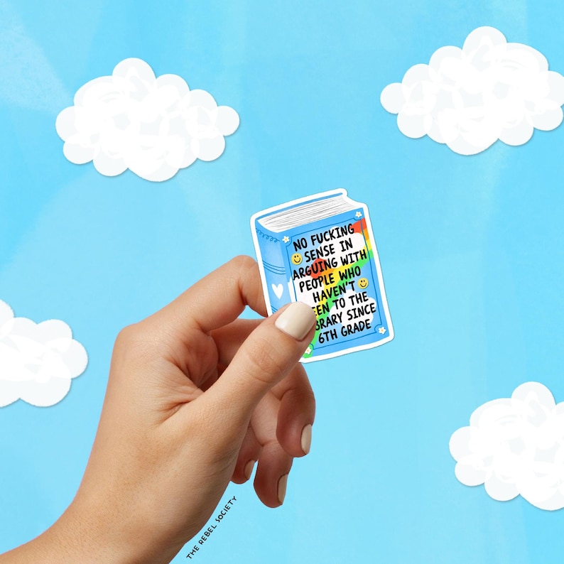May include: A blue sticker in the shape of a book with the text "NO FUCKING SENSE IN ARGUING WITH PEOPLE WHO HAVEN'T BEEN TO THE LIBRARY SINCE 6TH GRADE." The sticker is held in a hand against a blue sky background with white cloud cutouts.