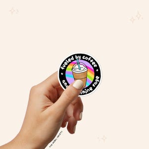 Puede incluir: Una pegatina en blanco y negro con un fondo de arco&iacute;ris y una taza de caf&eacute; helado de dibujos animados. El texto de la pegatina dice "fueled by coffee and sunshine rage".