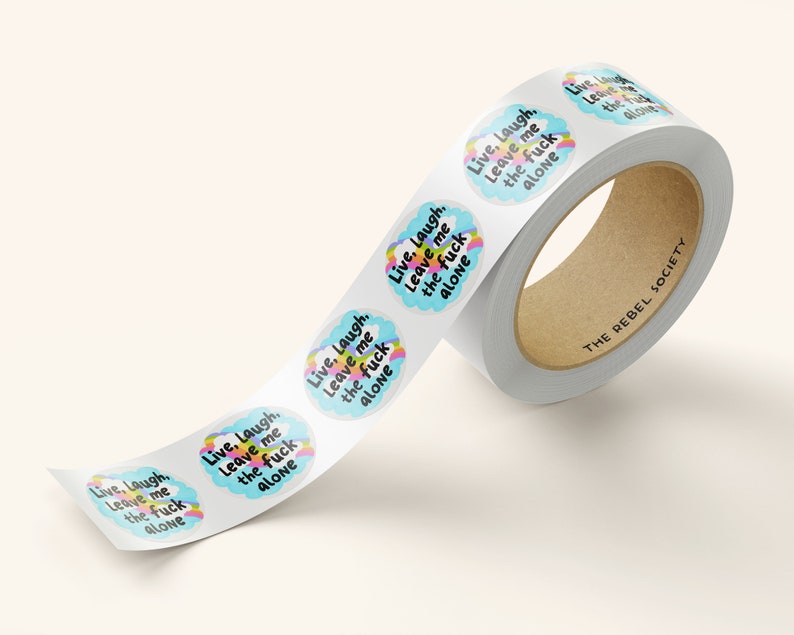 May include: A roll of stickers with the text "Live, Laugh, Leave me the fuck alone" in a white cloud with a rainbow arc. The text is in black and the background is blue. The stickers are on a white roll with the text "THE REBEL SOCIETY" printed on the roll.