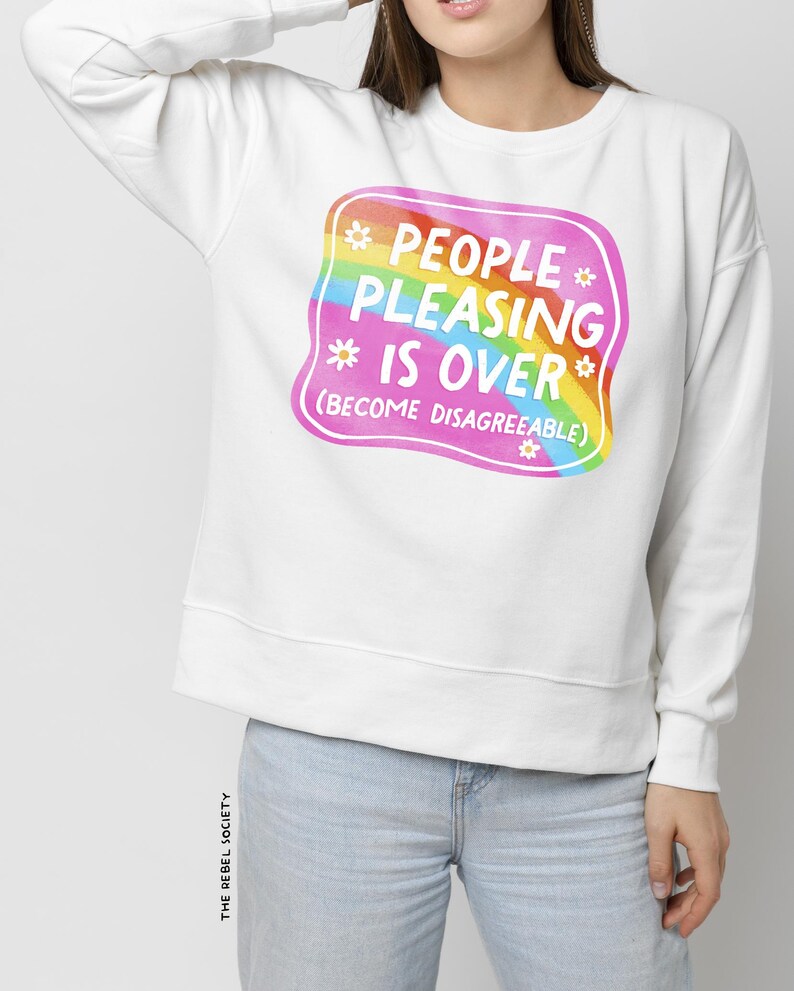 Puede incluir: Sudadera blanca con un gr&aacute;fico cuadrado rosa con un arco&iacute;ris y el texto "People Pleasing Is Over (Become Disagreeable)".