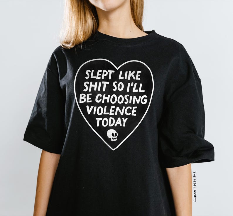 May include: Black t-shirt with a white heart-shaped graphic. The graphic includes the text "SLEPT LIKE SHIT SO I'LL BE CHOOSING VIOLENCE TODAY" and a small skull. The shirt is a casual style.