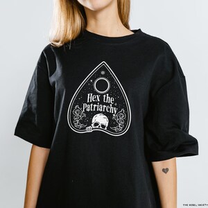 Może przedstawiać: Czarny T-shirt z białym nadrukiem planchette Ouija z tekstem "Hex the Patriarchy".