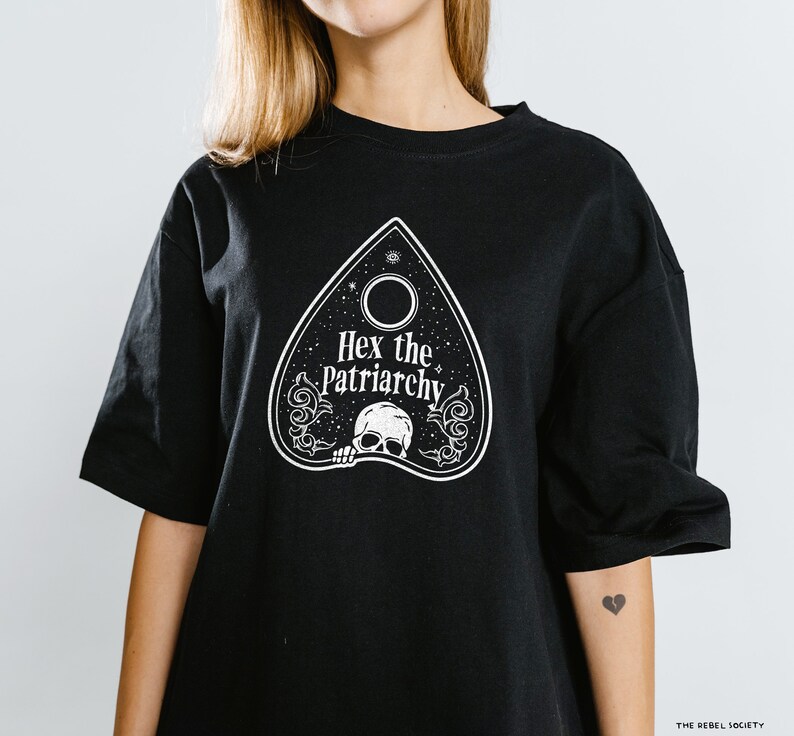 Może przedstawiać: Czarny T-shirt z białym nadrukiem planchette Ouija z tekstem "Hex the Patriarchy".