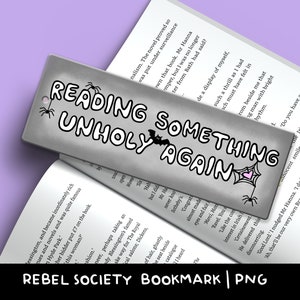 K&ouml;nnte beinhalten: Ein silbernes Lesezeichen mit einer Schwarzwei&szlig;illustration eines Spinnennetzes, einer Fledermaus und dem Text "Reading Something Unholy Again".