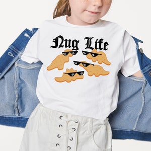 May include: White t-shirt with a black graphic that says "Nug Life" and features cartoon chicken nuggets wearing sunglasses.