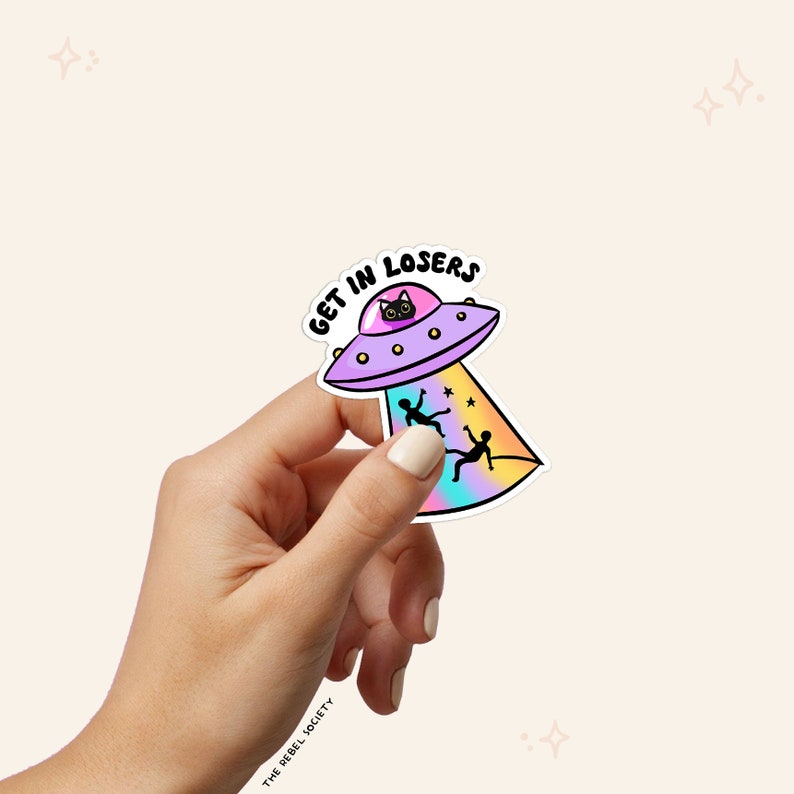 Puede incluir: Una pegatina con un OVNI de dibujos animados con un gato negro dentro. El OVNI tiene un rayo de color arco&iacute;ris que brilla sobre dos figuras de palo que caen del cielo. El texto "GET IN LOSERS" est&aacute; escrito en el OVNI.