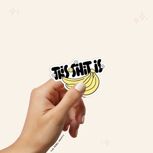 Puede incluir: Una pegatina negra y amarilla con el texto "This Shit Is" en una fuente divertida, con un racimo de pl&aacute;tanos amarillos y una carita sonriente.
