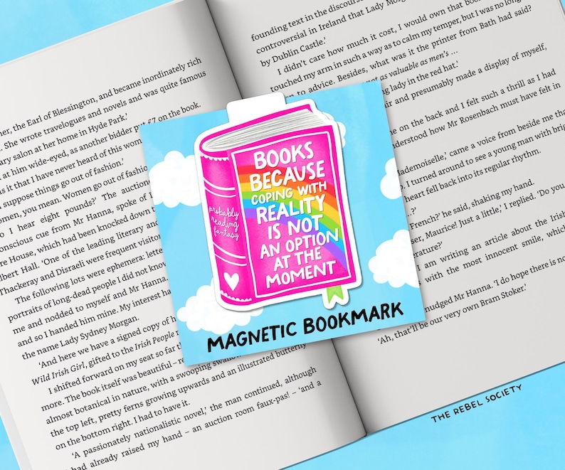 Puede incluir: Un marcap&aacute;ginas magn&eacute;tico con una ilustraci&oacute;n de libro rosa y el texto "BOOKS BECAUSE COPING WITH REALITY IS NOT AN OPTION AT THE MOMENT". Tiene un arco&iacute;ris y un coraz&oacute;n, sobre un cielo azul con nubes. Las palabras "MAGNETIC BOOKMARK" est&aacute;n en la parte inferior.
