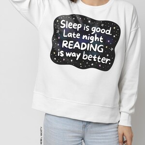 Pu&ograve; includere: Felpa bianca con grafica nera che recita "Sleep is good. Late night READING is way better." La grafica presenta un design a cielo stellato. La felpa &egrave; abbinata a jeans azzurri.
