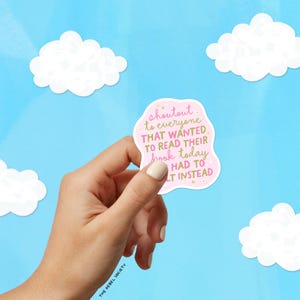 May include: A pink sticker with the text "shoutout to everyone THAT WANTED TO READ THEIR book today HAD TO LT INSTEAD" is held against a blue sky background with white cloud cutouts. The sticker is held by a hand.