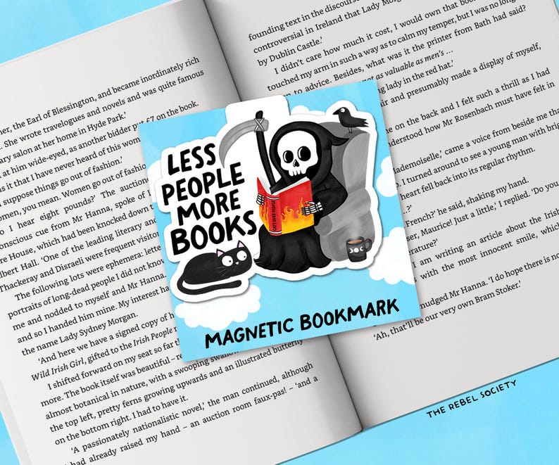 May include: A magnetic bookmark featuring a cartoon Grim Reaper reading a book with flames, a black cat, and a coffee cup. The text reads "LESS PEOPLE MORE BOOKS" and "MAGNETIC BOOKMARK". The bookmark is set against an open book.