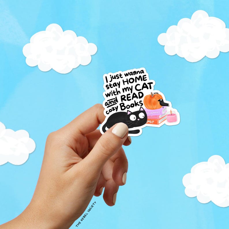 May include: A sticker featuring a black cat, a pumpkin, books, and a candle. The text reads, "I just wanna stay HOME with my CAT and READ cozy Books." The background is a light blue sky with white cloud shapes.