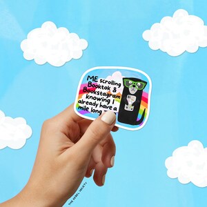 May include: A sticker featuring a black dog wearing green glasses and holding a phone. The sticker has text that reads "ME scrolling Booktok & Bookstagram knowing I already have a mile long." The background is blue with white clouds.