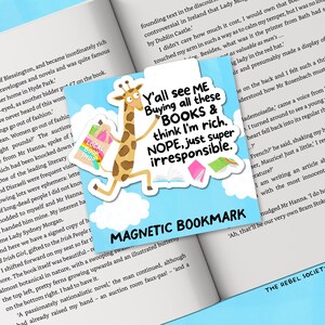 May include: A magnetic bookmark featuring a giraffe carrying shopping bags, with text reading "Y'all see ME Buying all these BOOKS & think I'm rich. NOPE, just super irresponsible." The bookmark is on an open book.