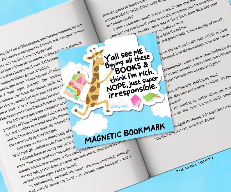 May include: A magnetic bookmark featuring a giraffe carrying shopping bags, with text reading "Y'all see ME Buying all these BOOKS & think I'm rich. NOPE, just super irresponsible." The bookmark is on an open book.