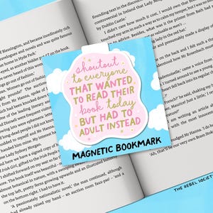 May include: A magnetic bookmark with a light blue background and a pink and white cloud-shaped design. The text reads "shoutout to everyone that wanted to read their book today but had to adult instead."