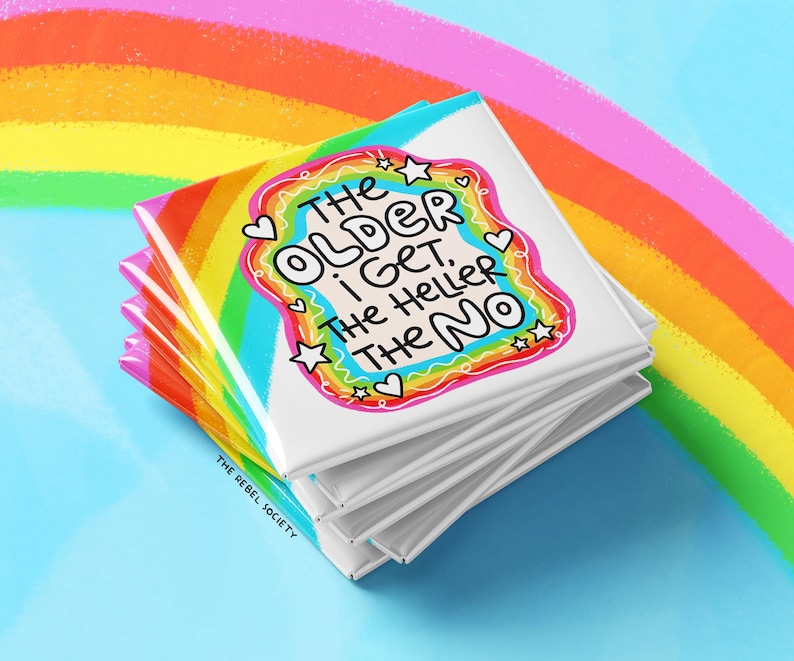 May include: A stack of square white coasters featuring a colorful rainbow border and the black text: THE OLDER I GET, THE HELLER THE NO. The design includes small white stars and hearts, with the text THE REBEL SOCIETY printed in the bottom corner.