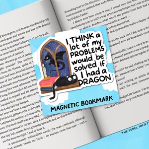 K&ouml;nnte beinhalten: Magnetischer Lesezeichen mit dem Text "I THINK a lot of my PROBLEMS would be solved if I had a DRAGON." Das Lesezeichen zeigt einen Drachen, eine schwarze Katze und ein Fensterdesign.