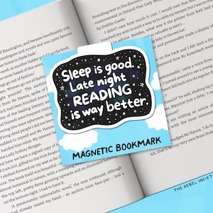 Pu&ograve; includere: Un segnalibro magnetico con la scritta "Sleep is good. Late night READING is way better." in un design in bianco e nero con sfondo stellato. Il segnalibro &egrave; sopra un libro aperto.