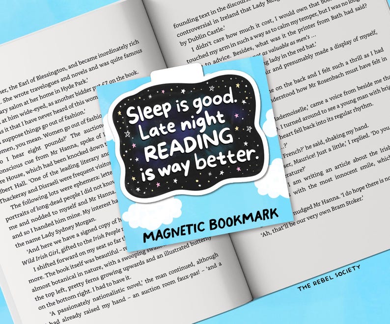 Pu&ograve; includere: Un segnalibro magnetico con la scritta "Sleep is good. Late night READING is way better." in un design in bianco e nero con sfondo stellato. Il segnalibro &egrave; sopra un libro aperto.