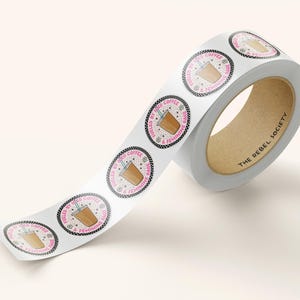 May include: A roll of white sticker tape with round stickers featuring a cartoon illustration of a coffee cup with the text "Fueled by the Coffee & Feminine Rage" in pink and black lettering.
