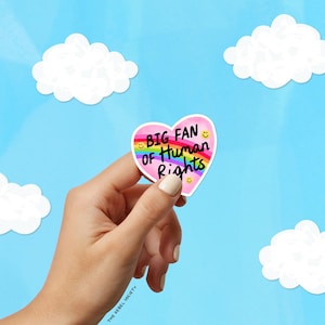 K&ouml;nnte beinhalten: Ein herzf&ouml;rmiger Aufkleber mit dem Text "BIG FAN of Human Rights" und einem Regenbogen-Design. Der Aufkleber wird von einer Hand vor einem blauen Himmel mit wei&szlig;en Wolken gehalten. Der Aufkleber hat einen rosa Rand und gelbe Smiley-Gesichter.