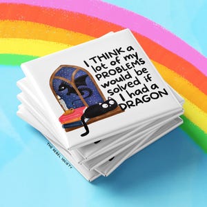 K&ouml;nnte beinhalten: Ein Stapel wei&szlig;er quadratischer Magnete mit einer skurrilen Illustration. Das Design zeigt eine schwarze Katze, einen Drachen und den Text "I THINK a lot of my PROBLEMS would be solved if I had a DRAGON." Der Hintergrund enth&auml;lt einen Regenbogen.