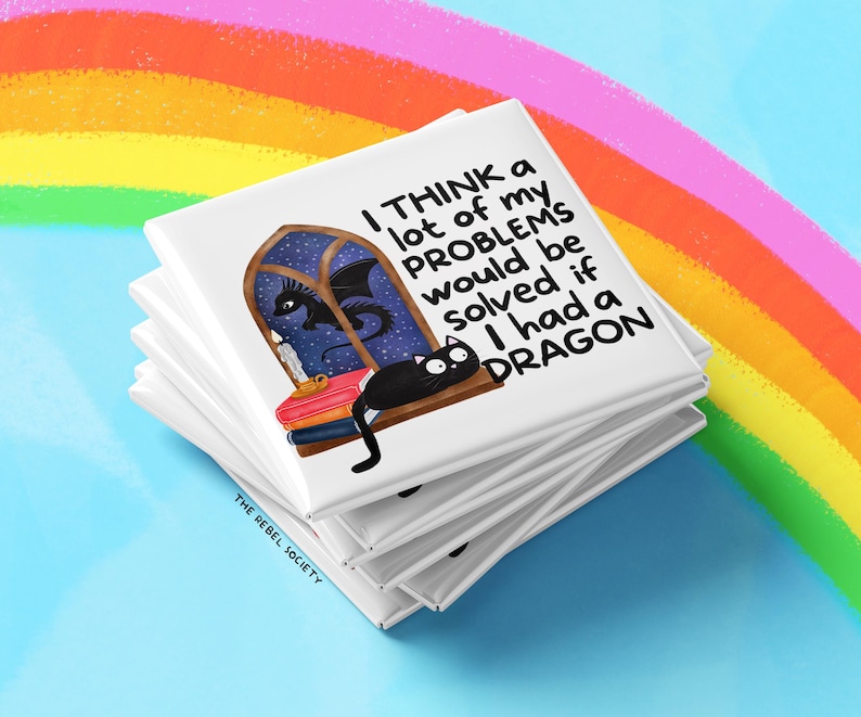 K&ouml;nnte beinhalten: Ein Stapel wei&szlig;er quadratischer Magnete mit einer skurrilen Illustration. Das Design zeigt eine schwarze Katze, einen Drachen und den Text "I THINK a lot of my PROBLEMS would be solved if I had a DRAGON." Der Hintergrund enth&auml;lt einen Regenbogen.
