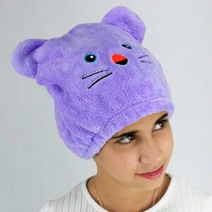 Könnte beinhalten: Lilafarbenes Mikrofaser-Haartuch mit einem niedlichen Comic-Katzenkopf. Das Handtuch ist so konzipiert, dass es hilft, das Haar schnell und einfach zu trocknen.