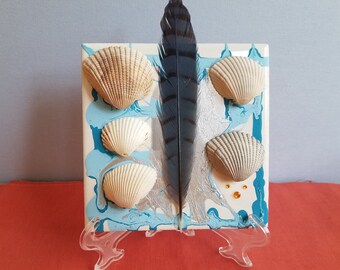 Muscheln und blaue Feder mit Strasssteinen und wirbelnder metallischer silberner und blauer Farbe auf einer 4 "x 4" Fliese."