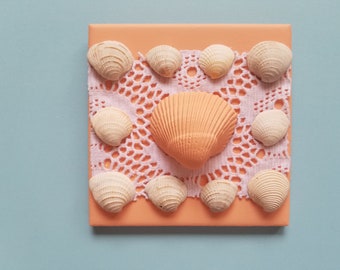 Pfirsichfarbene Muschel, umrandet von natürlichen Muscheln auf weißem Eyelet-Stoff auf 4 "x 4" -pfirsichfarbener Kachel