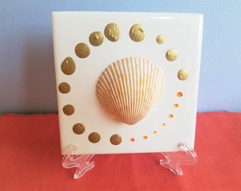 Herzmuschel in einem Kreis aus metallischen Goldfarbenpunkten und orangefarbenen Strasssteinen auf einer 4 "x 4" Fliese