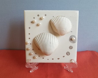 Weiße Muscheln mit Perlen und metallisch silber gemalten Tupfen auf einer 10 cm x 10 cm großen Fliese