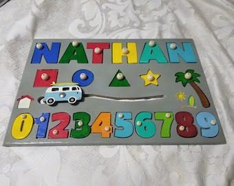 Può includere: Un puzzle in legno con il nome "NATHAN" scritto in lettere colorate. Il puzzle include anche i numeri da 0 a 9, forme e un piccolo furgone blu. I pezzi del puzzle sono tenuti in posizione da pioli in legno.