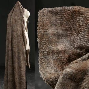 May include: A draped, textured fabric in shades of brown and tan, with a scale-like pattern. The fabric is draped over a mannequin, with a close-up view showing the detailed texture and color variations. The overall effect suggests a reptile skin or similar material.
