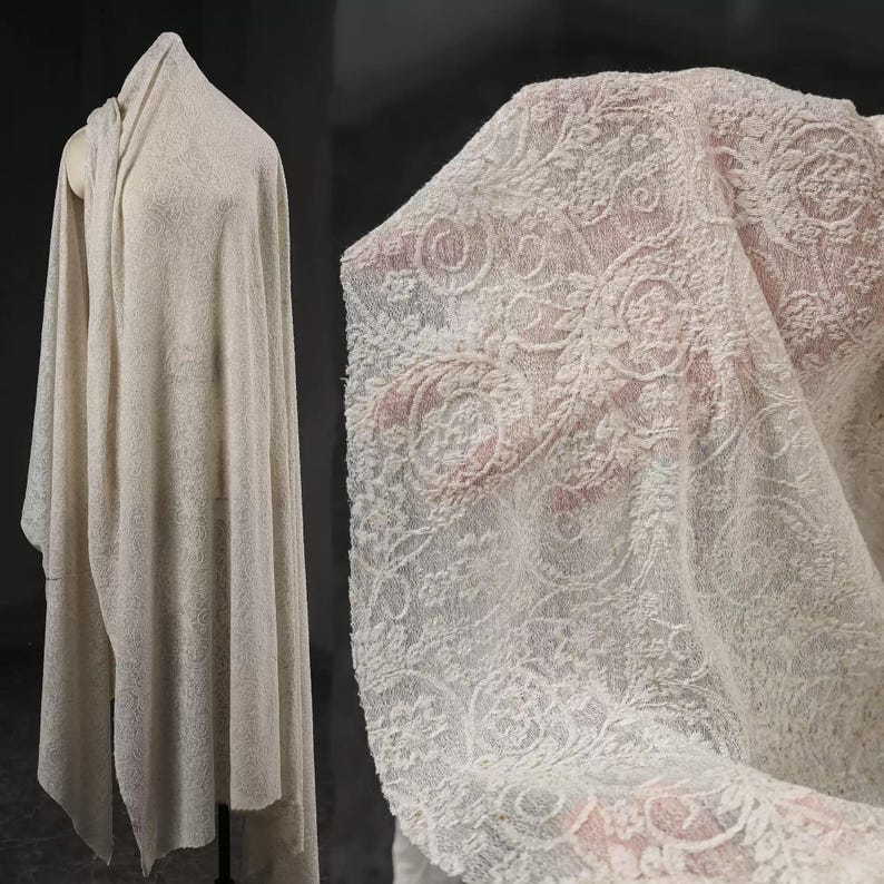 May include: Off-white fabric with a delicate floral lace pattern. The fabric is draped over a mannequin and also held up to show the intricate details of the lace. The fabric appears soft and lightweight, suitable for various craft projects.